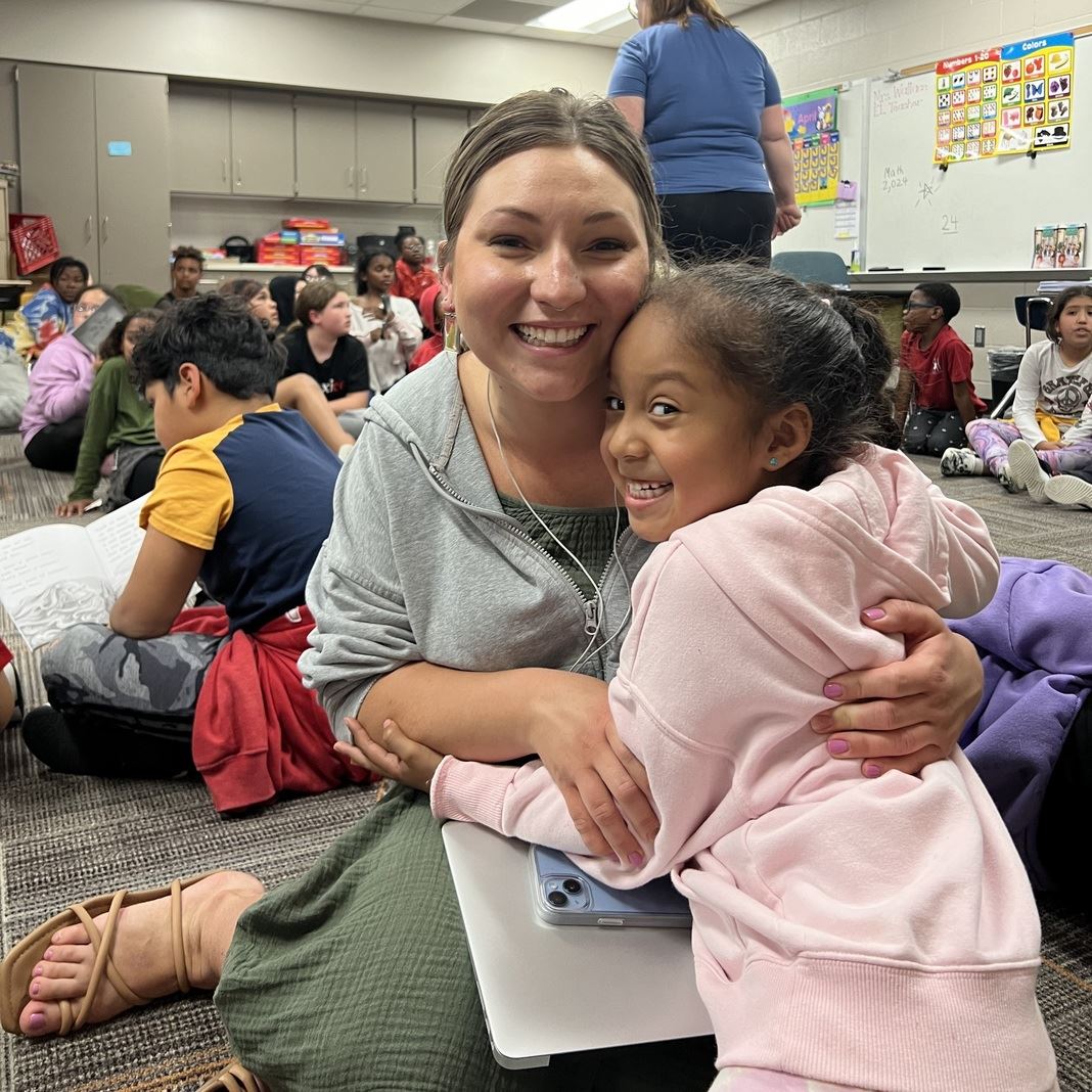 Breanna Stohs sits on the floor with a student